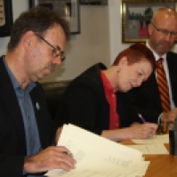 Cee signs the terms of settlement for the caregiver's offer in parliament on behalf of NZNO after two years of negotiations. John Ryall negotiator from E tū picture at left.
